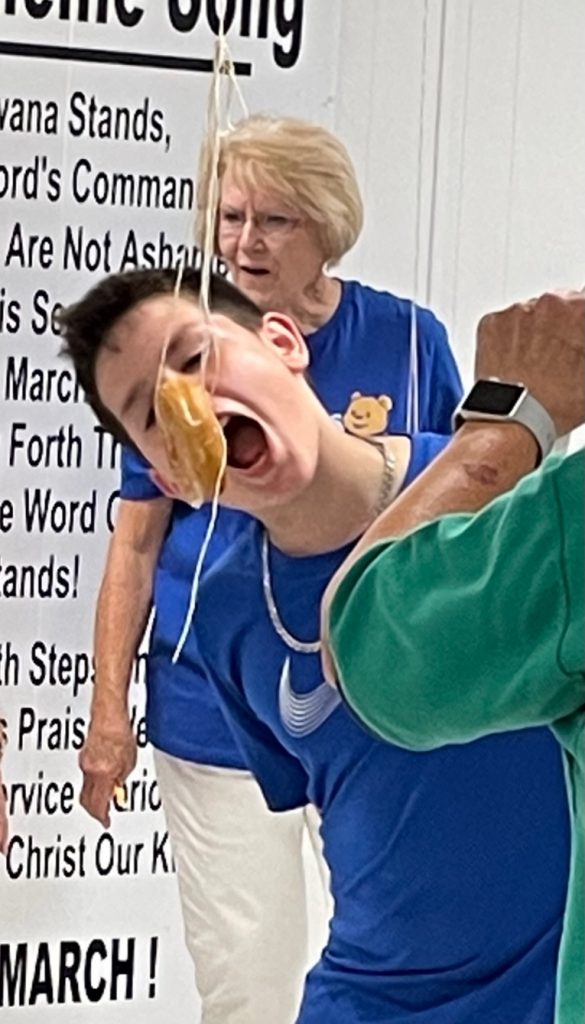 Child eats donut on a string.